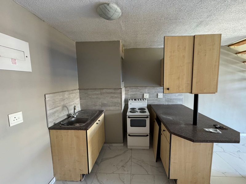 Compact kitchen featuring laminate cabinetry, tiled backsplash, stainless steel sink, and a freestanding stove, with tiled flooring throughout.