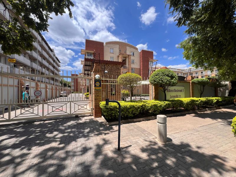Front entrance view of Hillcrest Boulevard 1 apartment complex, featuring secure gated access, brick facade, and well-maintained landscaping.