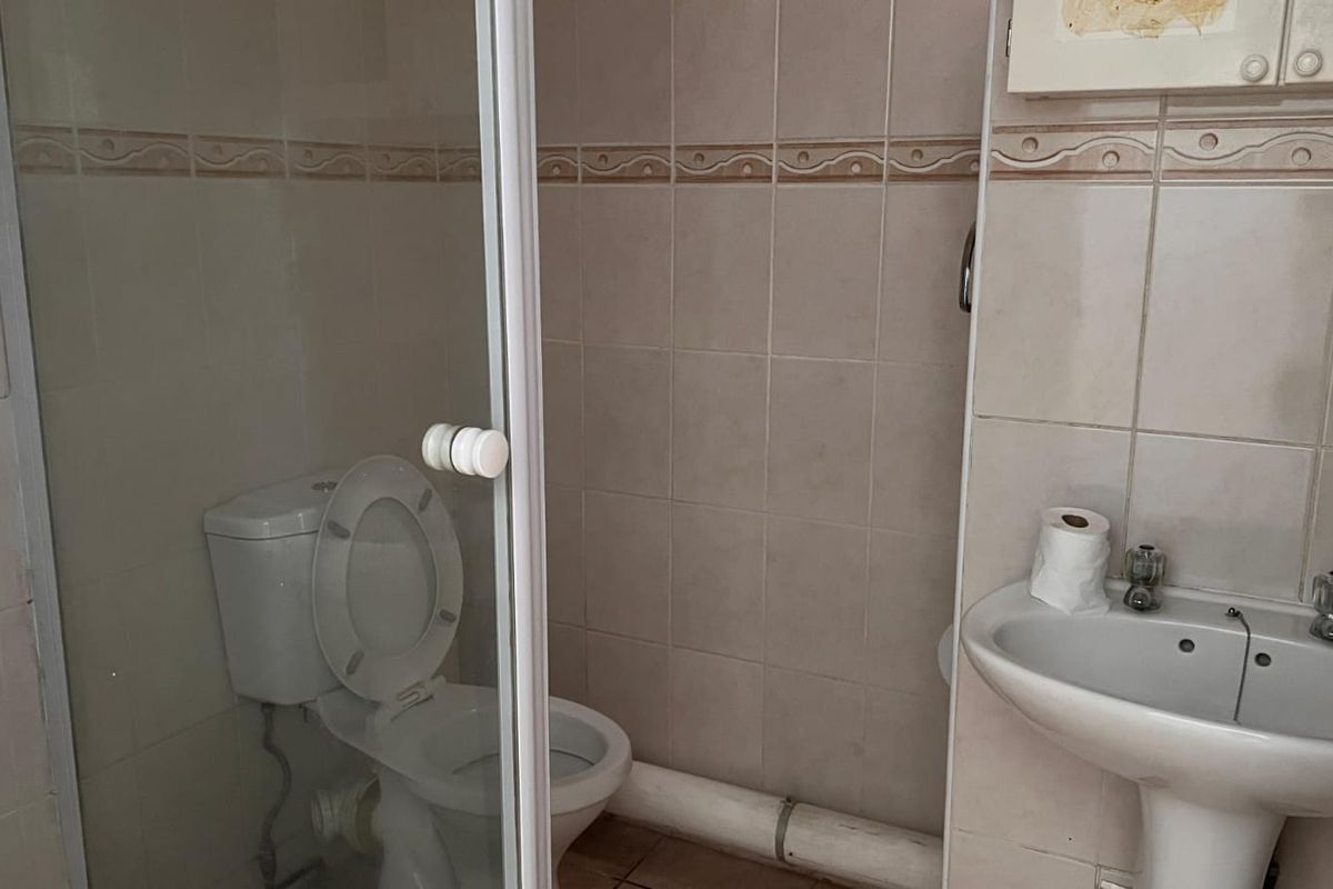 A compact bathroom featuring a pedestal basin, toilet, and shower enclosure with neutral wall tiling and visible plumbing.