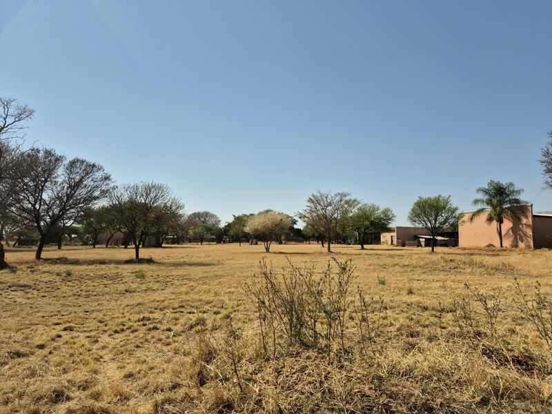A wide-angle view of the farm property featuring expansive dry pasture land and existing outbuildings under a clear blue sky.