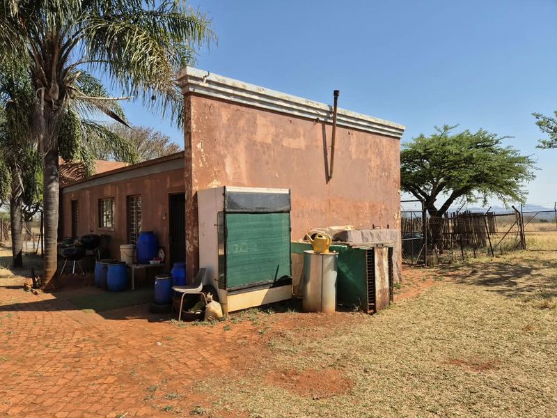 Rear view of a farm building featuring weathered masonry walls, a parapet roofline, and brick paved outdoor area.