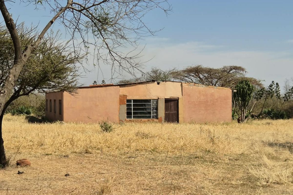 A detached single-story farm building with plastered masonry walls and metal window frames, situated in a rural landscape.
