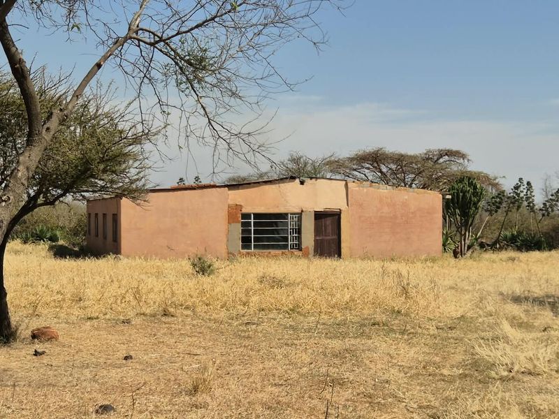 A detached single-story farm building with plastered masonry walls and metal window frames, situated in a rural landscape.
