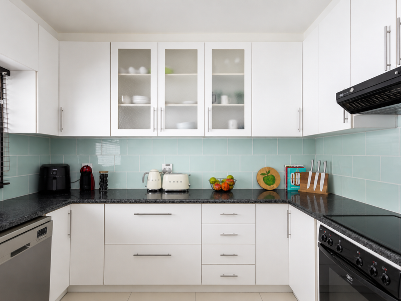A modern, well-maintained kitchen featuring white cabinetry, black granite countertops, a light blue subway tile backsplash, and integrated appliances.