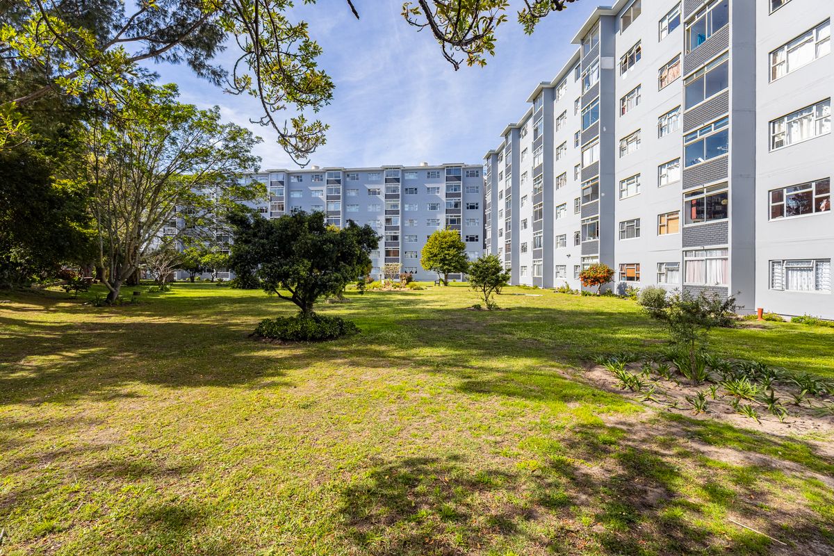 A view of the rear apartment building facade overlooking a well-maintained communal garden area with mature trees and lawn.