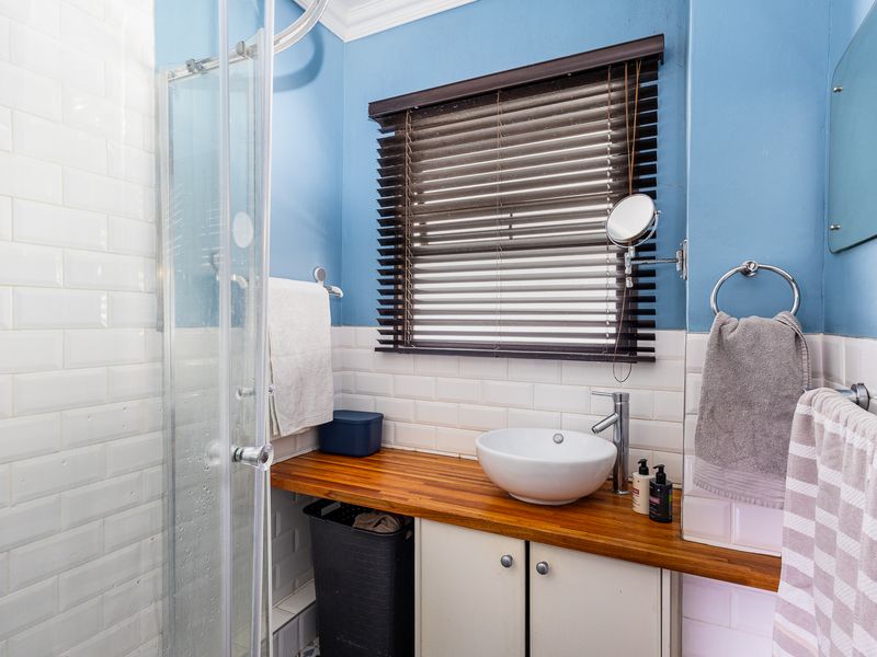 A well-maintained bathroom featuring a modern vessel sink on a wooden vanity countertop, a glass shower enclosure, and classic white subway tile wall finishes.