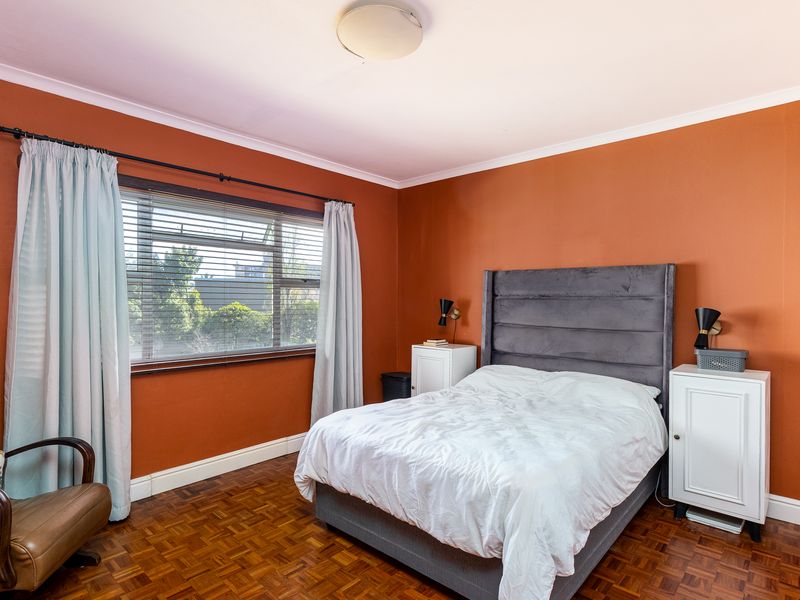 A well-proportioned bedroom featuring classic parquet flooring, coved ceilings, and a large window with fitted blinds, offering a comfortable and functional living space.