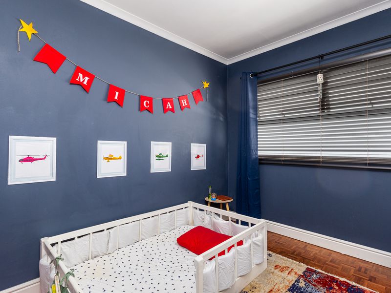 A well-maintained bedroom featuring dark blue walls, classic parquet flooring, and venetian blinds, offering a cozy and functional living space.