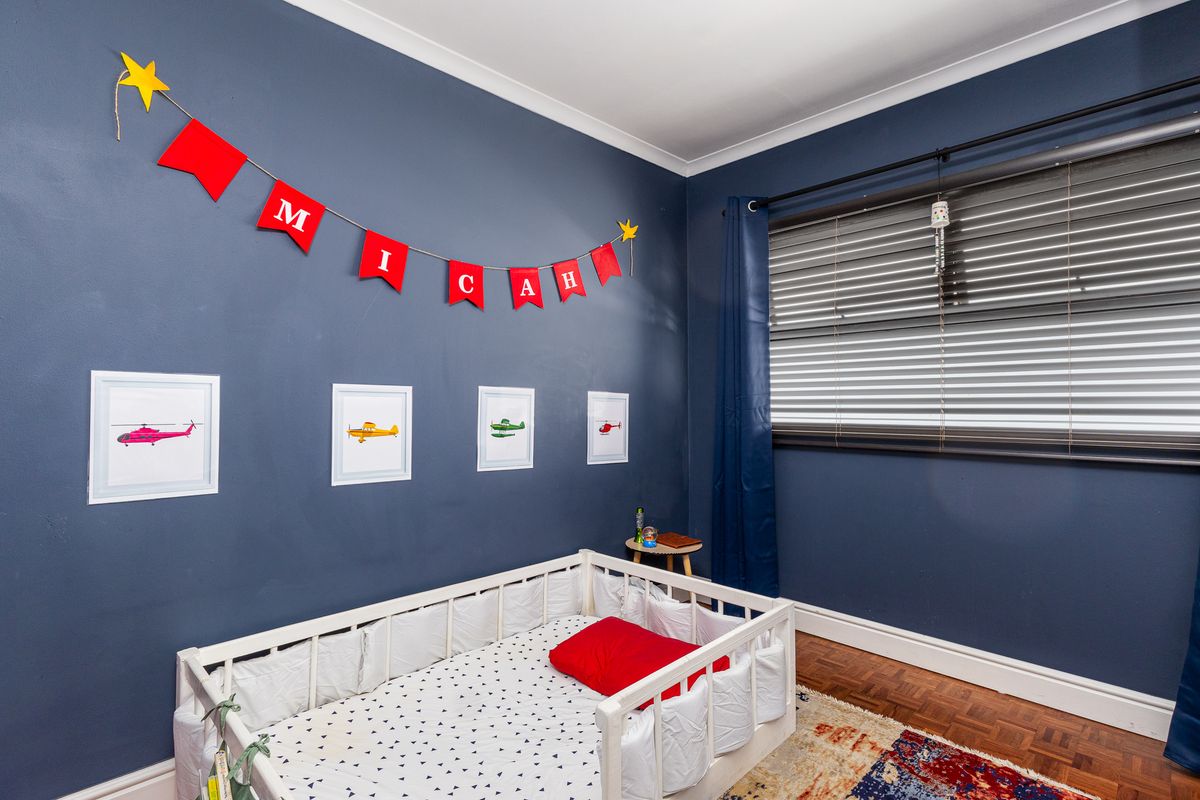 A well-maintained bedroom featuring dark blue walls, classic parquet flooring, and venetian blinds, offering a cozy and functional living space.