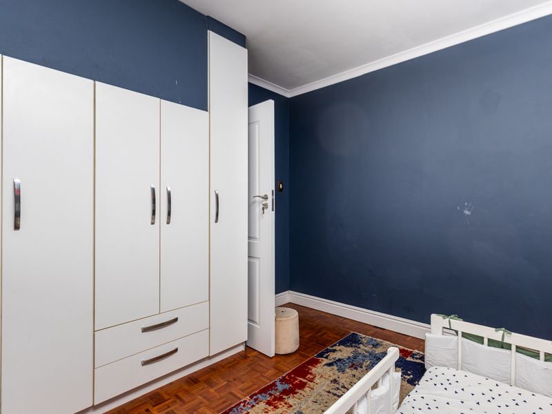 Bedroom featuring dark blue accent walls, built-in white cabinetry, and classic parquet flooring.