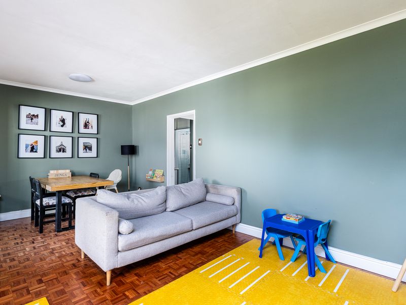 A well-maintained living area featuring classic parquet flooring, coved ceilings, and neutral green wall finishes, providing a versatile space for relaxation and dining.