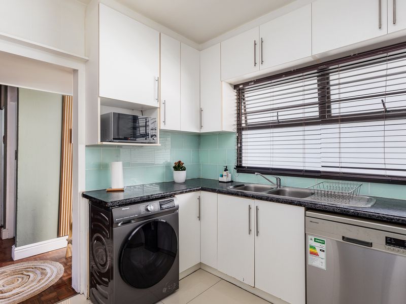 A functional kitchen featuring white cabinetry, dark laminate countertops, a double basin sink, and a light blue tiled backsplash with integrated appliance spaces.