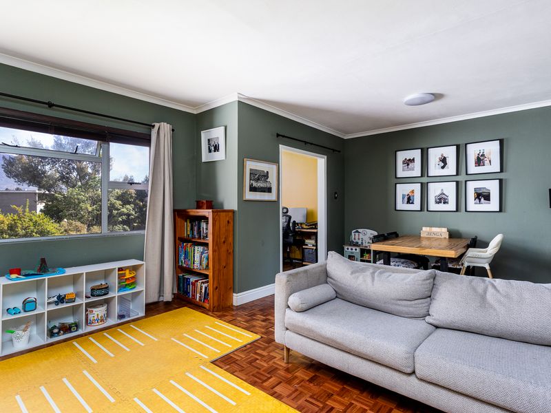 A well-maintained living room featuring classic parquet flooring, coved cornicing, and large windows providing natural light and pleasant exterior views.