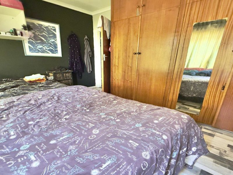 A bedroom featuring a large built-in wooden wardrobe with a central mirror and a floating wall shelf for storage.