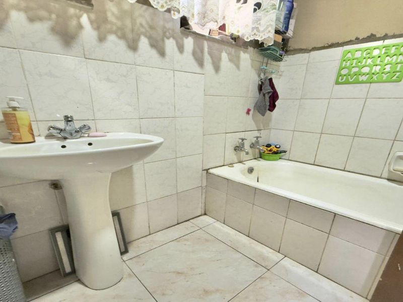 A functional bathroom featuring a pedestal basin and a built-in bathtub with tiled walls and flooring, requiring cosmetic updates and maintenance.