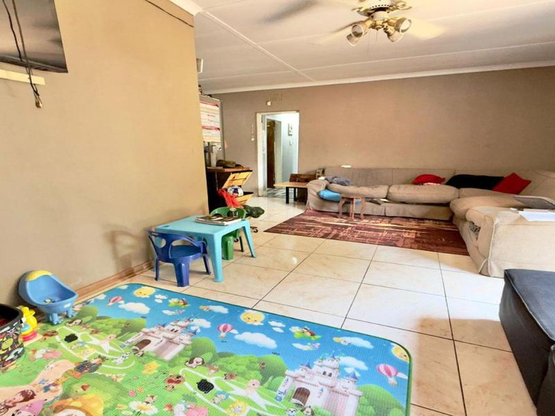 A spacious living room featuring neutral wall tones, large floor tiles, and a ceiling fan, offering a versatile layout for family living.