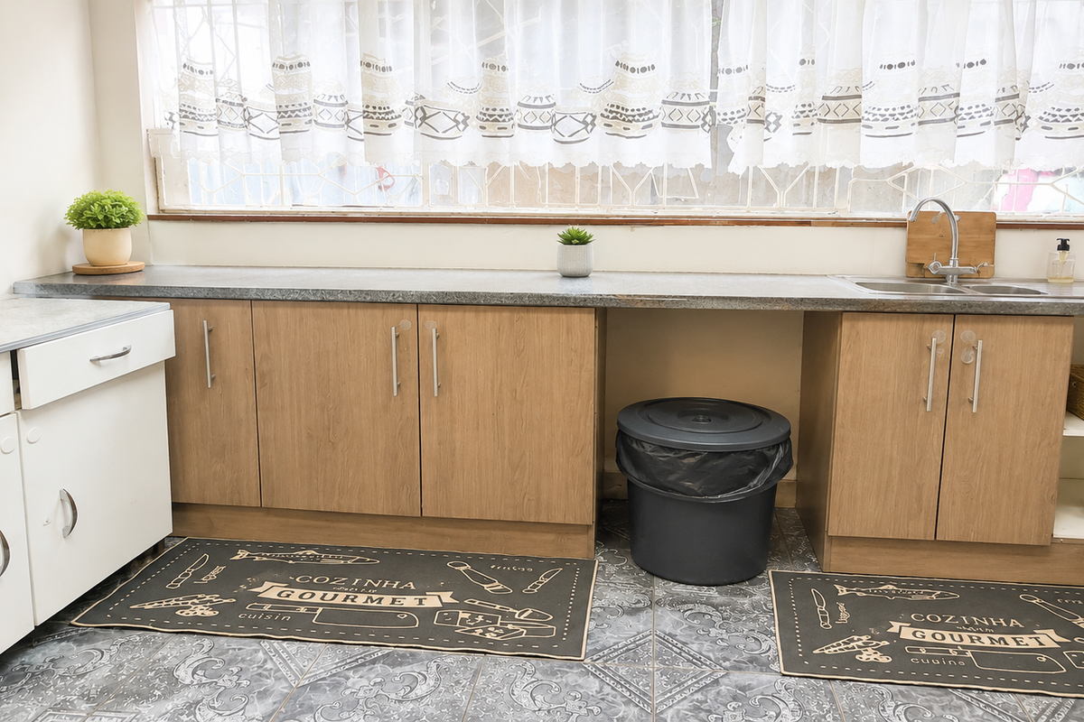 A functional kitchen area featuring wood-finish cabinetry, a laminate countertop, stainless steel sink, and patterned tiled flooring.