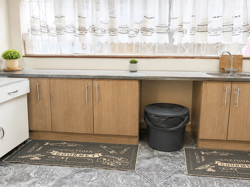 A functional kitchen area featuring wood-finish cabinetry, a laminate countertop, stainless steel sink, and patterned tiled flooring.