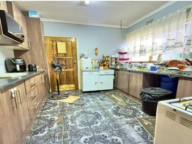 A functional kitchen featuring wood-look laminate cabinetry, dark countertops, and tiled flooring, offering potential for a modern cosmetic update.