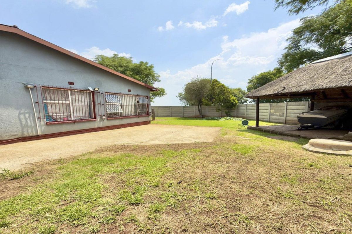 Spacious rear yard featuring a paved driveway, a traditional thatched lapa, and perimeter precast concrete walling.