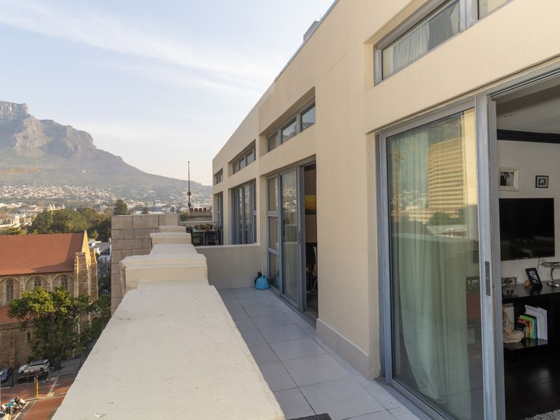 A spacious balcony featuring tiled flooring and sliding glass doors, offering expansive views of the city and mountain landscape.