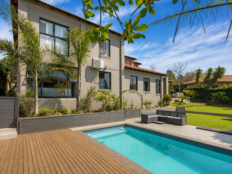 A well-maintained rear garden featuring a swimming pool, timber decking, and a paved patio area adjacent to the main residence.