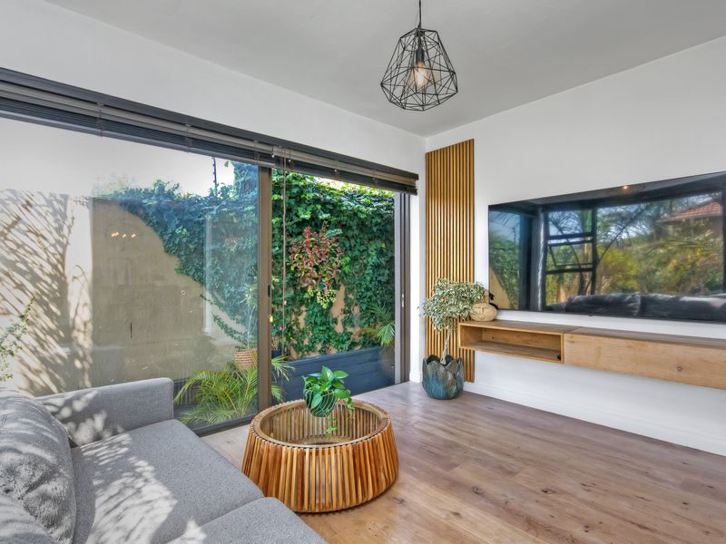 Modern living room featuring timber slat wall accents, a floating media console, laminate wood flooring, and large sliding doors opening to a private garden.