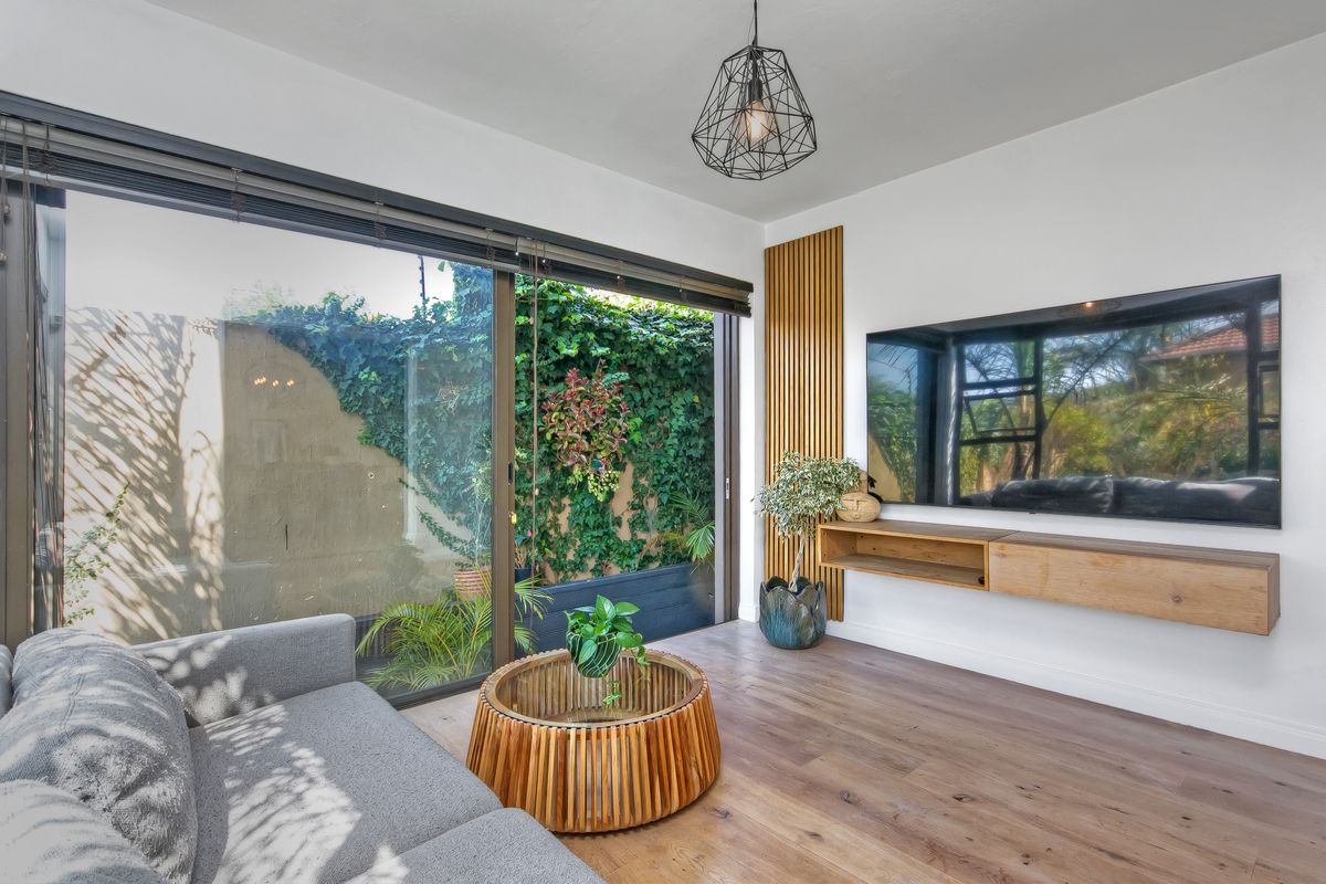 Modern living room featuring timber slat wall accents, a floating media console, laminate wood flooring, and large sliding doors opening to a private garden.