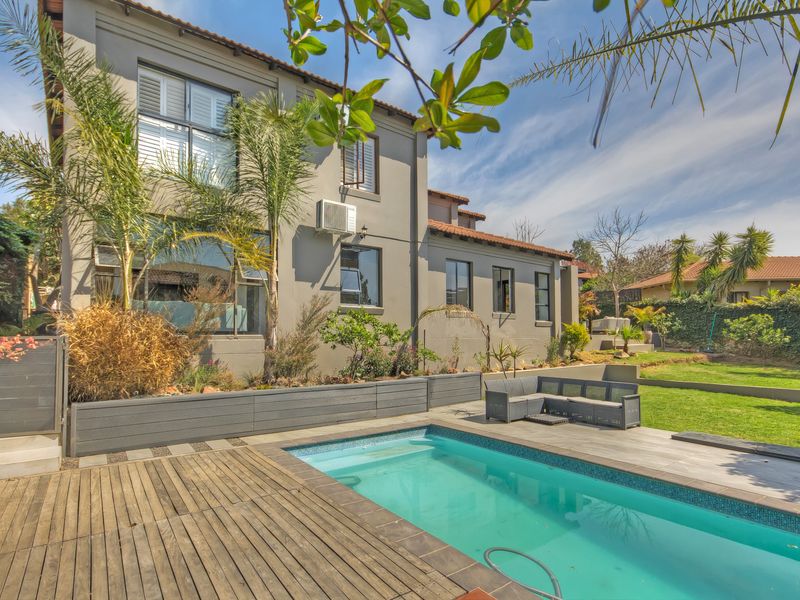 Rear exterior view featuring a swimming pool, wooden decking, raised garden beds, and a well-maintained garden area.