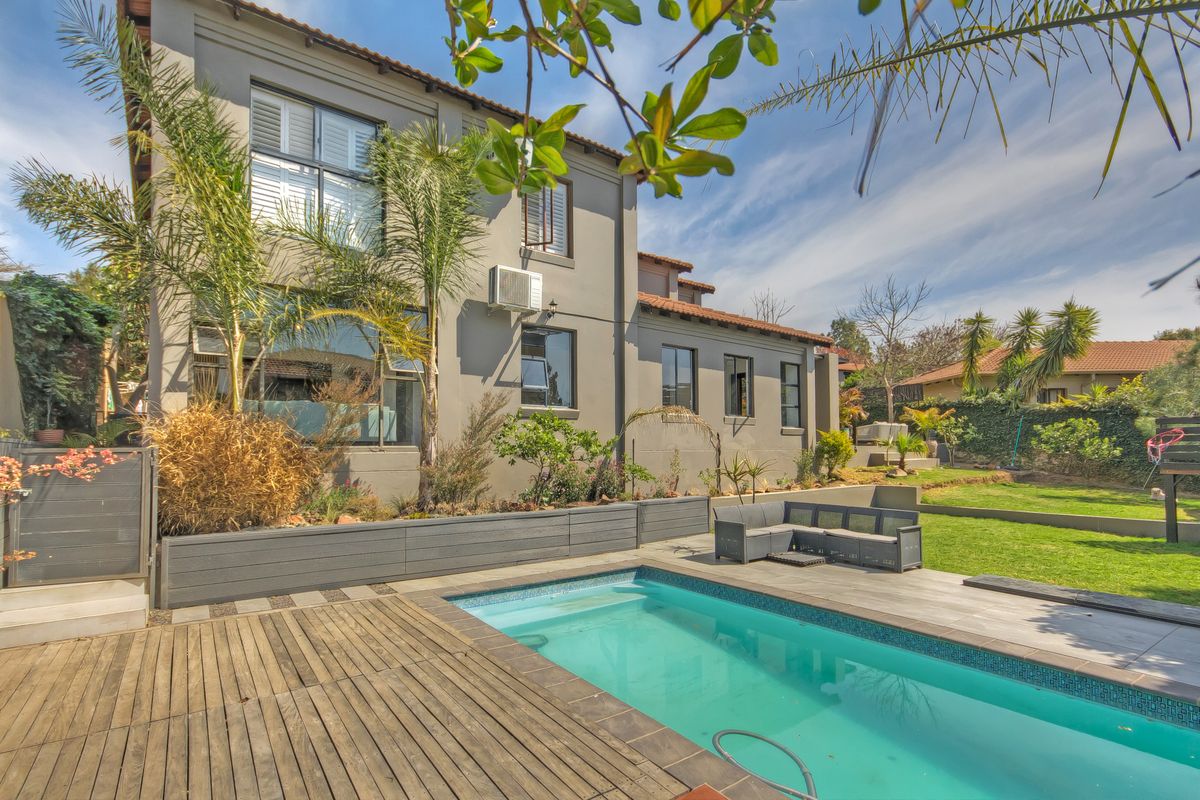 Rear exterior view featuring a swimming pool, wooden decking, raised garden beds, and a well-maintained garden area.