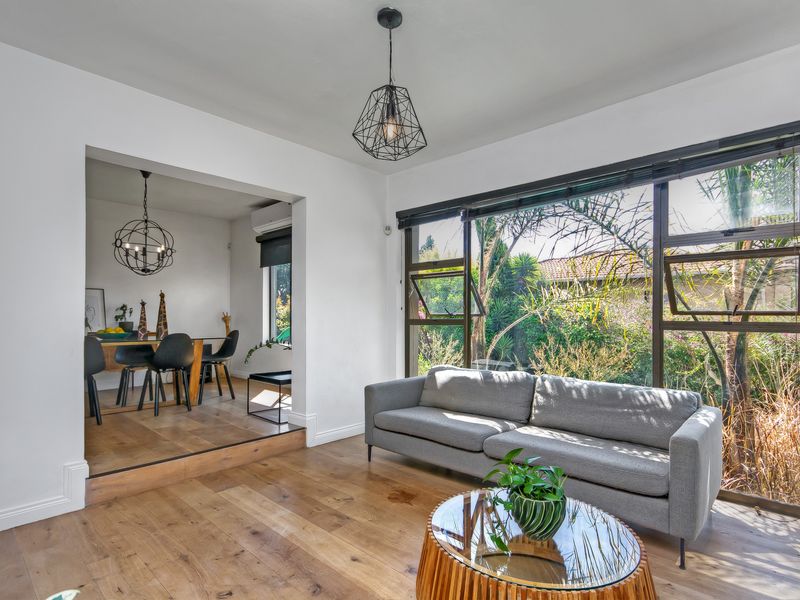 Bright open-plan living and dining area featuring hardwood flooring, large windows with garden views, and a raised dining platform.