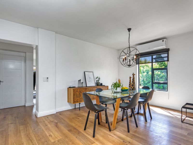 Bright and modern dining area featuring warm hardwood flooring, a contemporary pendant light, and a split-system air conditioning unit.