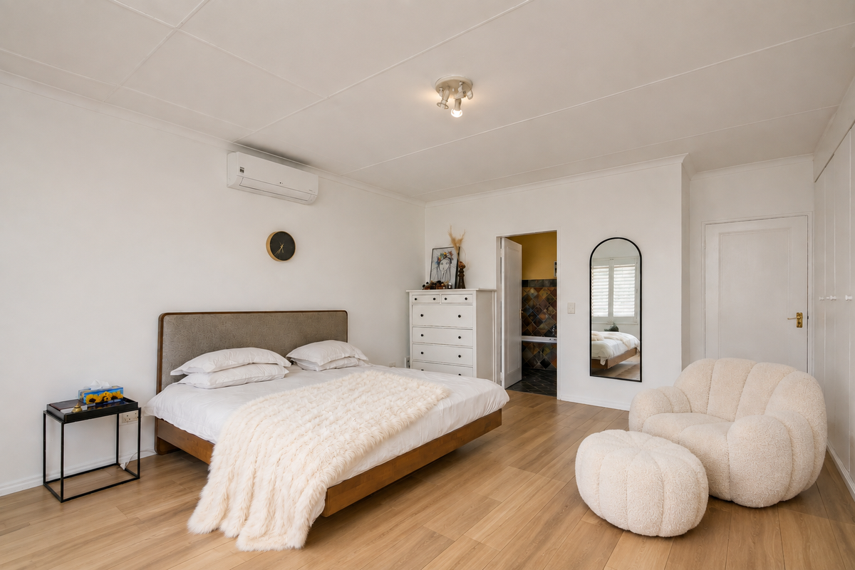 Spacious bedroom featuring light laminate flooring, built-in cupboards, and a wall-mounted air conditioning unit, with an adjoining bathroom visible.