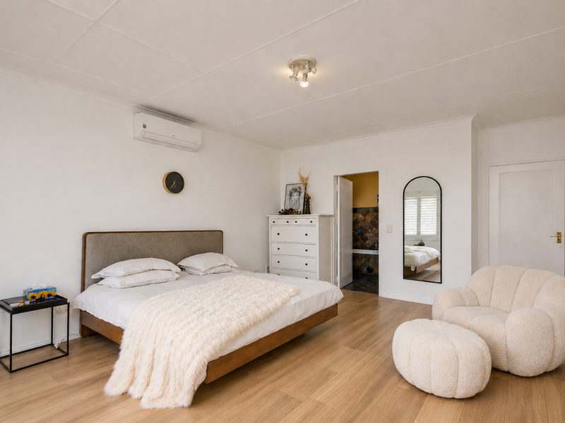 Spacious bedroom featuring light laminate flooring, built-in cupboards, and a wall-mounted air conditioning unit, with an adjoining bathroom visible.