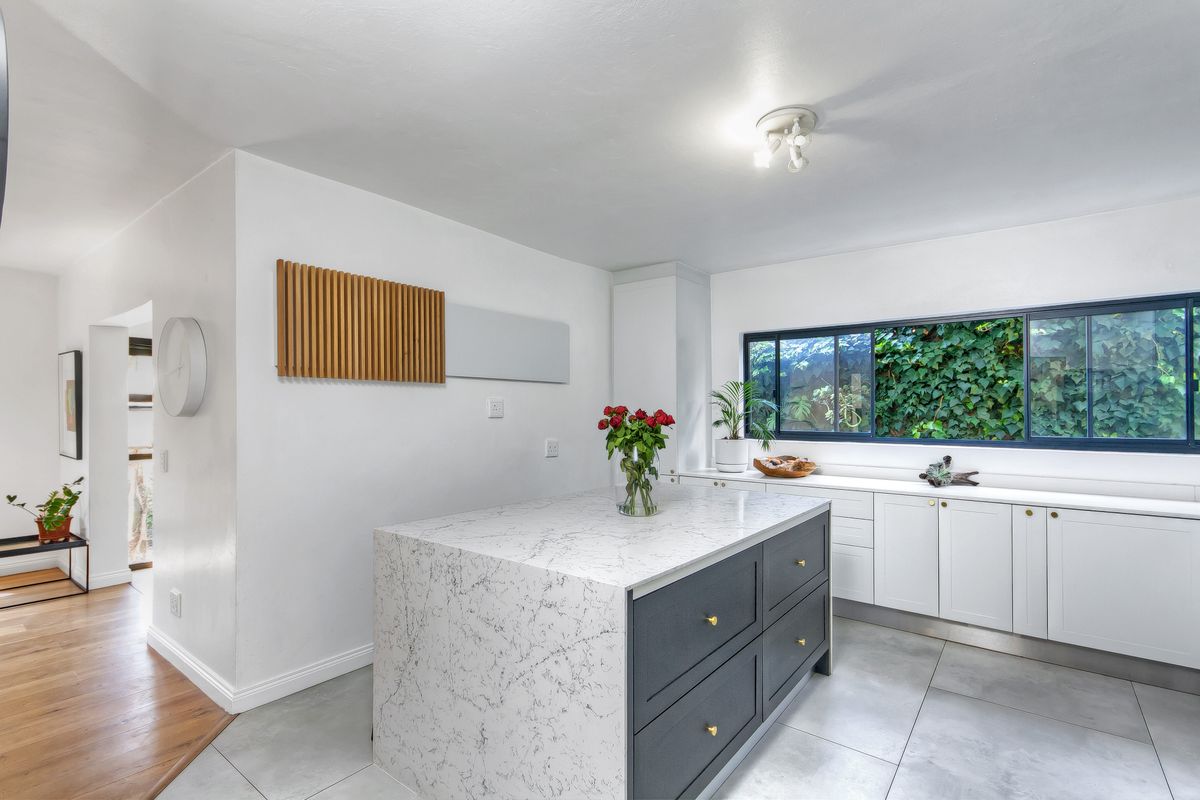 Modern kitchen featuring a central island with marble-look countertop, sleek cabinetry, and large windows overlooking a lush garden.