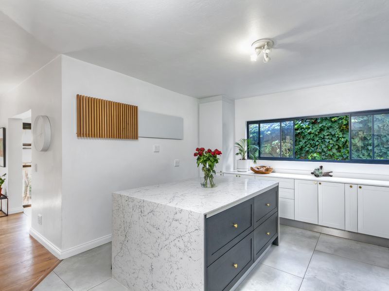 Modern kitchen featuring a central island with marble-look countertop, sleek cabinetry, and large windows overlooking a lush garden.