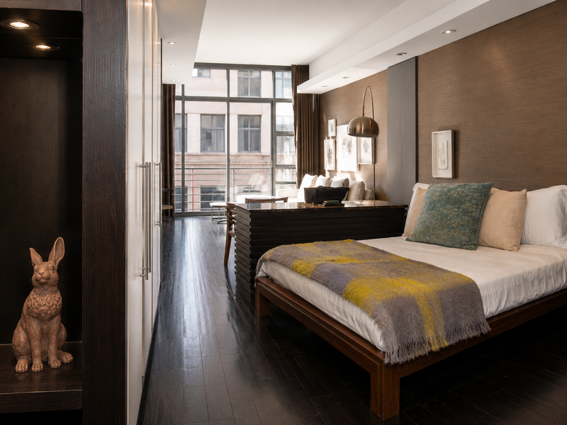 A modern bedroom featuring dark hardwood floors, built-in cabinetry, and textured wall finishes with large windows providing natural light.