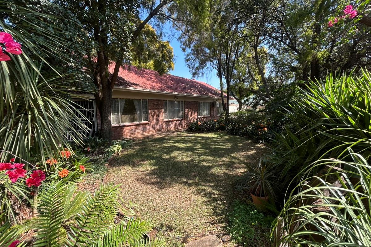 A view of the rear brick facade of the house, featuring a tiled roof and a well-established garden with mature trees.