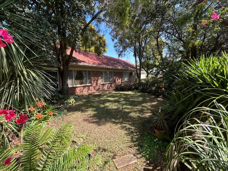 A view of the rear brick facade of the house, featuring a tiled roof and a well-established garden with mature trees.