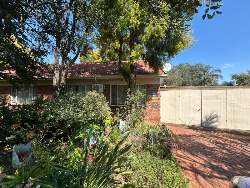 Front view of a brick house featuring a tiled roof, paved driveway, and an attached garage, surrounded by established garden landscaping.