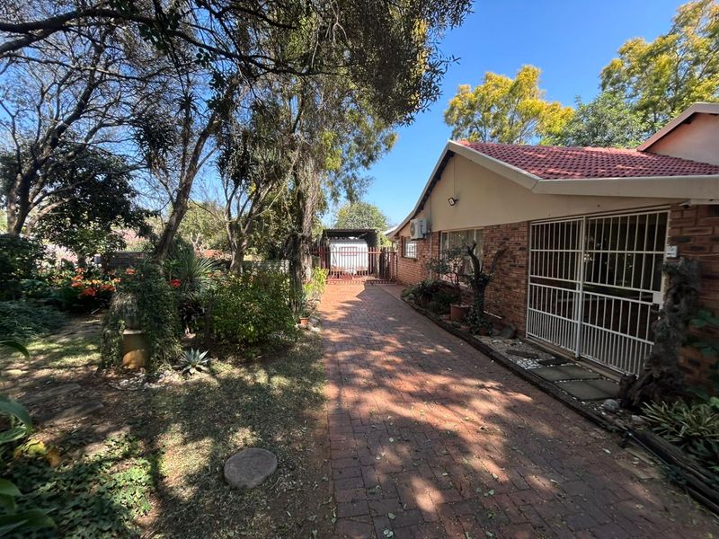 Rear exterior view of the property featuring a brick-paved driveway, established garden, and secure access points with fitted security gates.