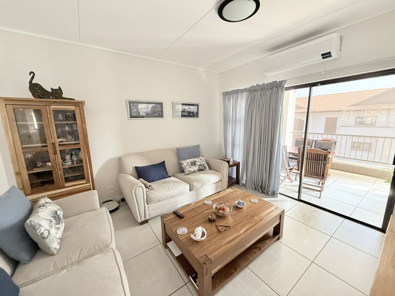 A bright living room featuring tiled flooring, a wall-mounted air conditioning unit, and large sliding glass doors providing access to an outdoor balcony area.