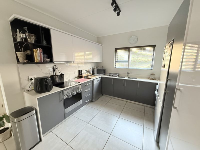 Modern kitchen featuring sleek grey and white cabinetry, integrated electric oven and hob, tiled flooring, and ample counter space with a functional layout.