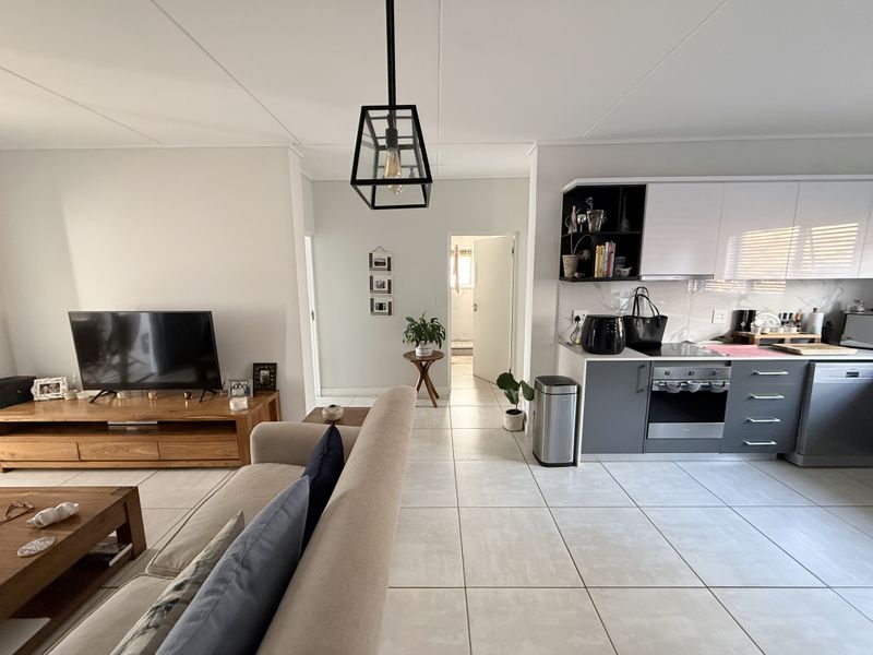 Open-plan living area featuring a modern kitchen with built-in oven, hob, and sleek cabinetry, seamlessly flowing into the lounge space with tiled flooring.