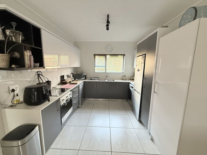 Modern kitchen featuring sleek two-tone cabinetry, integrated appliances, tiled flooring, and a functional layout with ample storage and workspace.