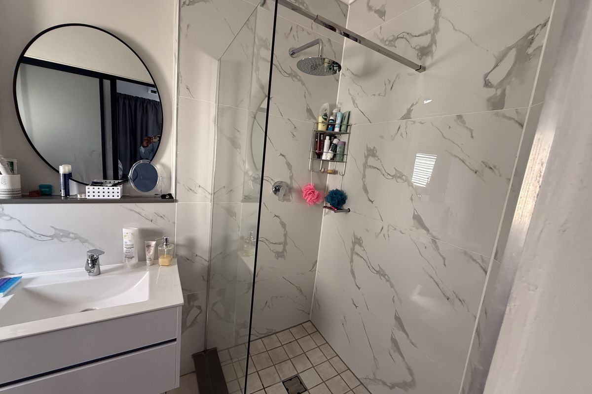 Modern bathroom featuring a vanity with basin, walk-in shower with glass screen, rain shower head, and elegant marble-look wall tiling.