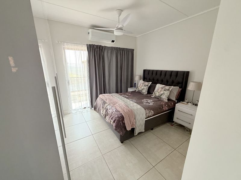 A well-maintained bedroom featuring tiled flooring, a ceiling fan, a split-system air conditioner, and a sliding glass door providing access to the outdoors.