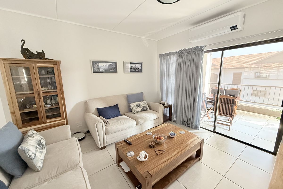 A bright living room featuring tiled flooring, a wall-mounted air conditioning unit, and large sliding glass doors providing access to an outdoor balcony area.