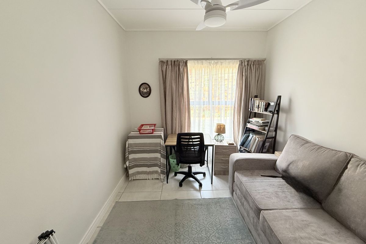 A functional bedroom featuring tiled flooring and a ceiling fan, currently utilized as a home office and living space.