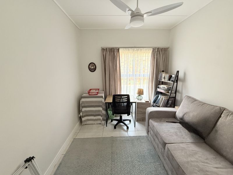 A functional bedroom featuring tiled flooring and a ceiling fan, currently utilized as a home office and living space.
